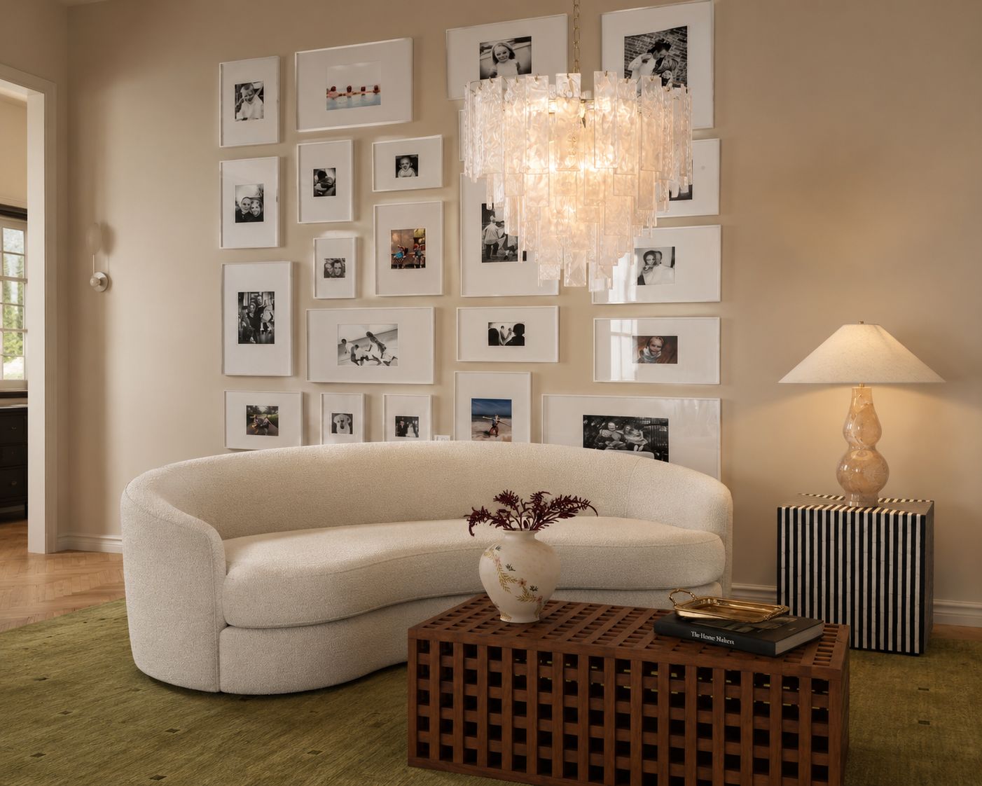 A sitting room with a curved white boucle sofa, a lattice timber coffee table and a Murano chandelier in front of a gallery wall of white-framed photographs.